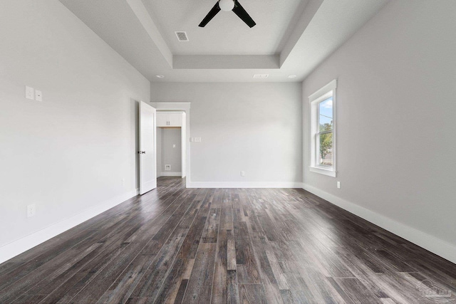 unfurnished room featuring ceiling fan, dark wood-type flooring, and a tray ceiling