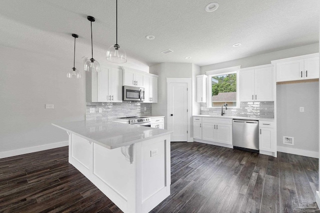 kitchen with dark hardwood / wood-style floors, pendant lighting, sink, stainless steel appliances, and white cabinets