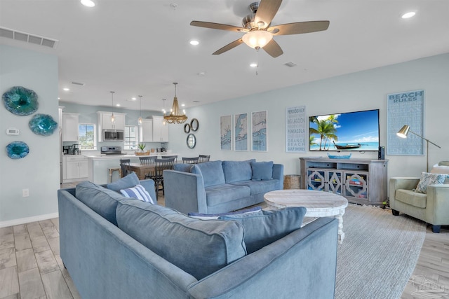 living area featuring ceiling fan with notable chandelier, light wood-style floors, visible vents, and recessed lighting