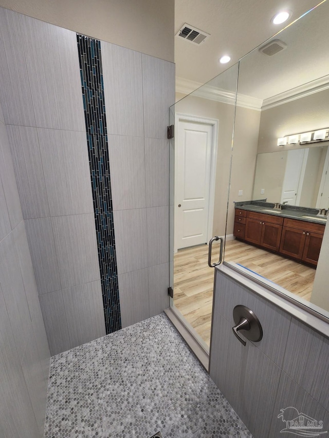 bathroom with hardwood / wood-style floors, vanity, a tile shower, and crown molding