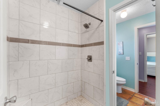 bathroom with toilet, a tile shower, and a textured ceiling