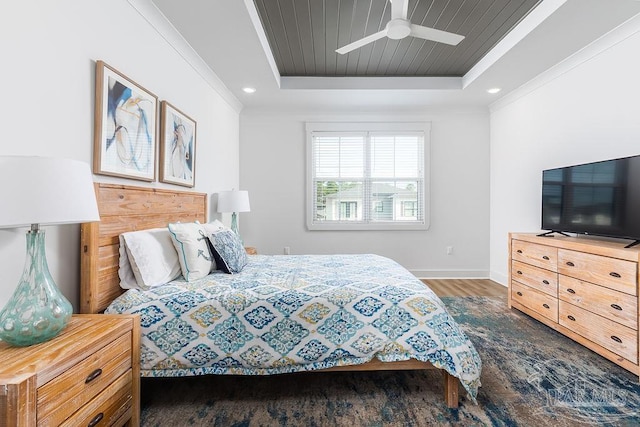 bedroom with ceiling fan, a tray ceiling, dark wood-type flooring, and ornamental molding