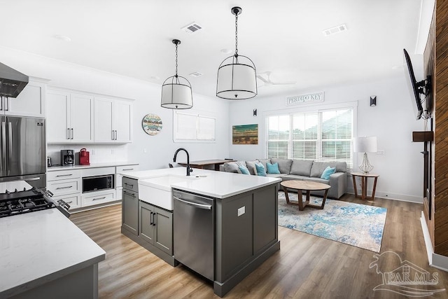 kitchen with a kitchen island with sink, wood-type flooring, white cabinets, hanging light fixtures, and appliances with stainless steel finishes