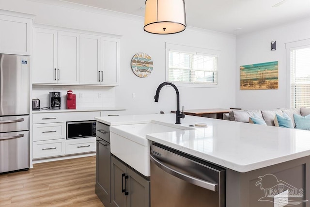 kitchen with a kitchen island with sink, light wood-type flooring, stainless steel appliances, backsplash, and white cabinets