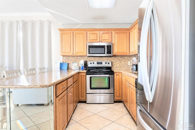 kitchen with light tile patterned floors, kitchen peninsula, appliances with stainless steel finishes, and a kitchen breakfast bar