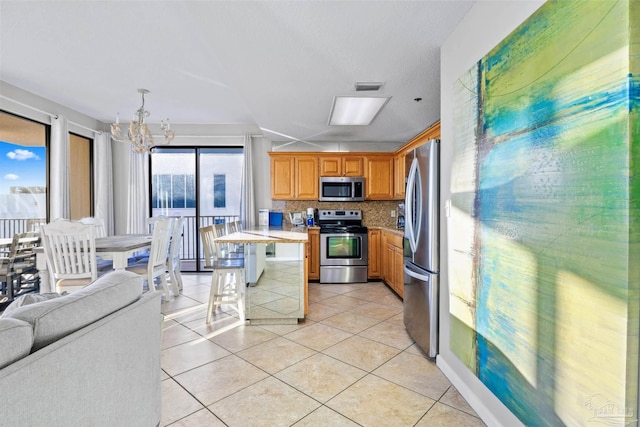 kitchen featuring tasteful backsplash, an inviting chandelier, a kitchen breakfast bar, stainless steel appliances, and light tile patterned floors