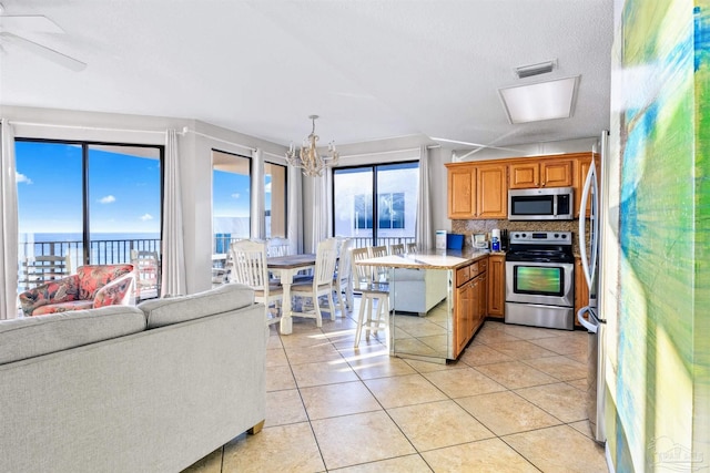 kitchen featuring light tile patterned floors, appliances with stainless steel finishes, backsplash, decorative light fixtures, and a chandelier