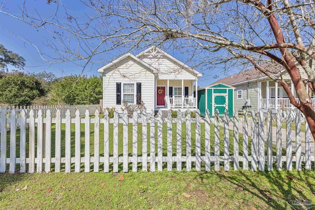 view of front of home with a storage shed, a porch, a fenced front yard, and a front yard