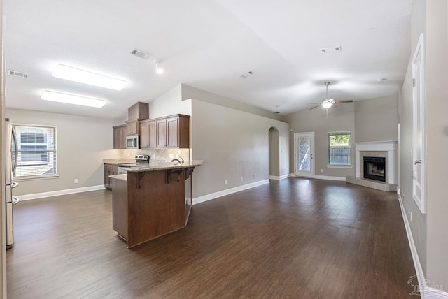 kitchen with dark hardwood / wood-style floors, kitchen peninsula, vaulted ceiling, a breakfast bar, and appliances with stainless steel finishes