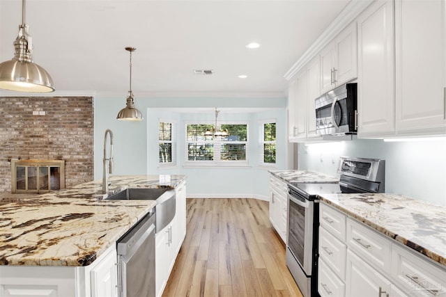 kitchen featuring appliances with stainless steel finishes, light wood-type flooring, decorative light fixtures, white cabinets, and ornamental molding