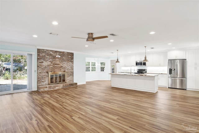 unfurnished living room featuring ceiling fan, sink, a brick fireplace, light hardwood / wood-style flooring, and ornamental molding