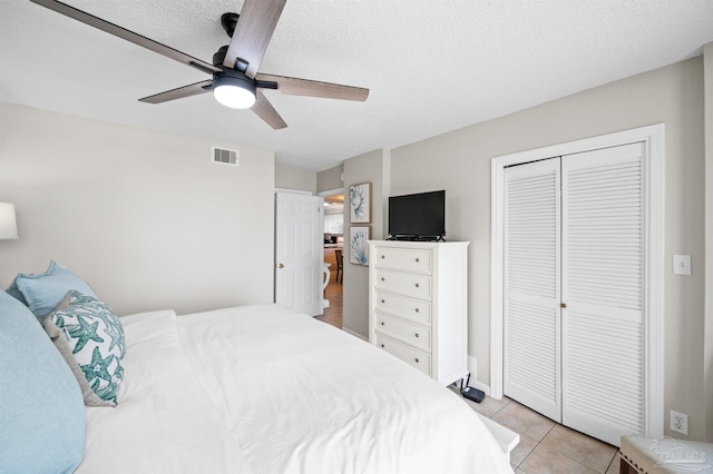 tiled bedroom with ceiling fan, a textured ceiling, and a closet