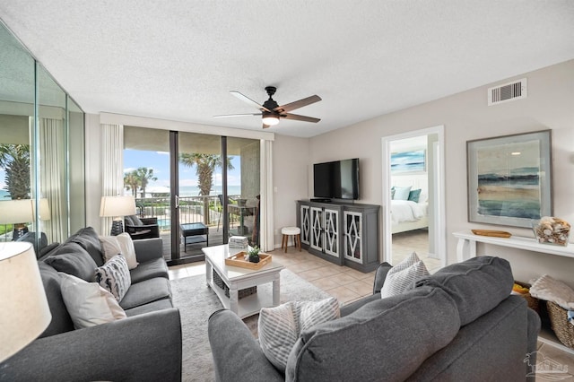 tiled living room with ceiling fan, a wall of windows, and a textured ceiling