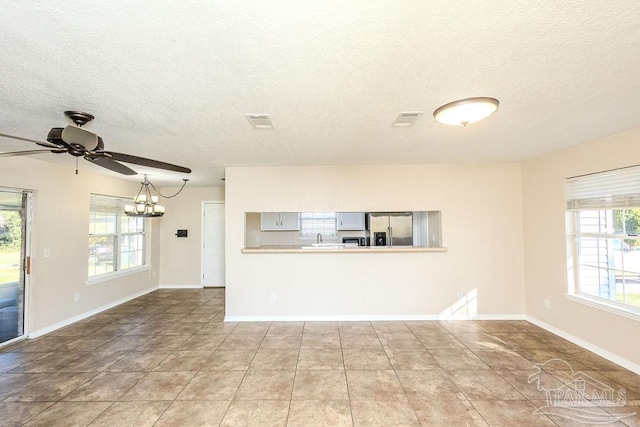 unfurnished living room featuring a textured ceiling, plenty of natural light, and ceiling fan with notable chandelier