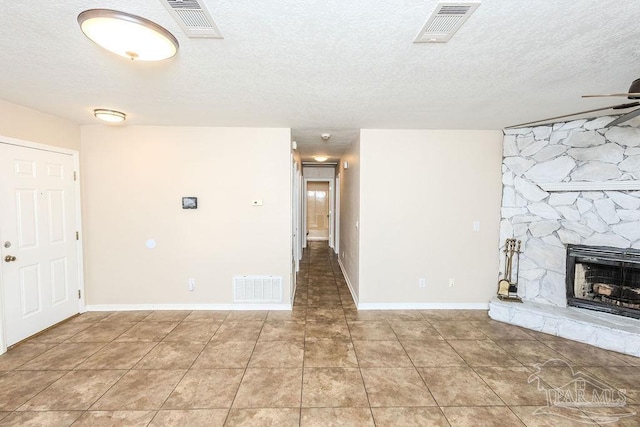 unfurnished living room with a stone fireplace, ceiling fan, light tile patterned flooring, and a textured ceiling