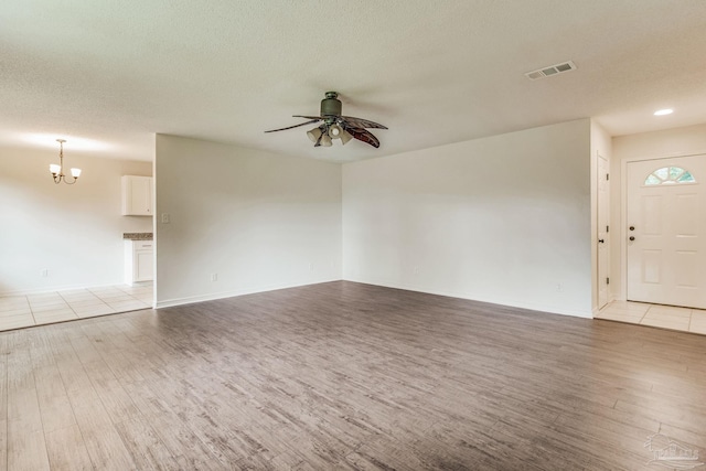 unfurnished living room with a textured ceiling, ceiling fan with notable chandelier, and light wood-type flooring