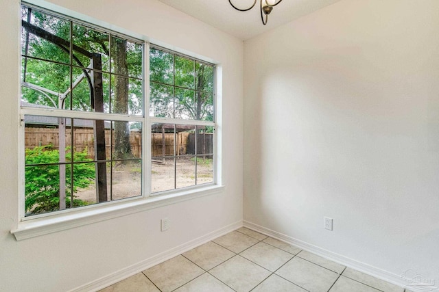 empty room with a wealth of natural light, light tile patterned flooring, and a chandelier