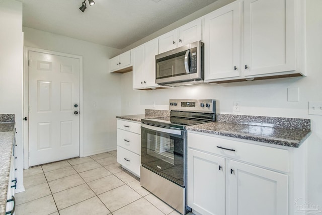 kitchen featuring white cabinets, light tile patterned floors, stainless steel appliances, and dark stone countertops