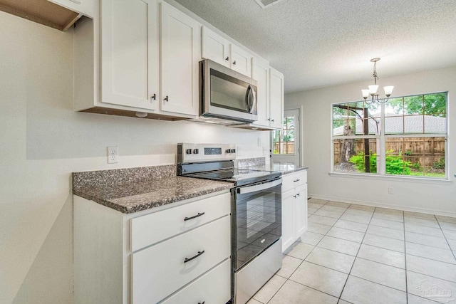 kitchen featuring white cabinetry, stainless steel appliances, a notable chandelier, dark stone countertops, and light tile patterned flooring