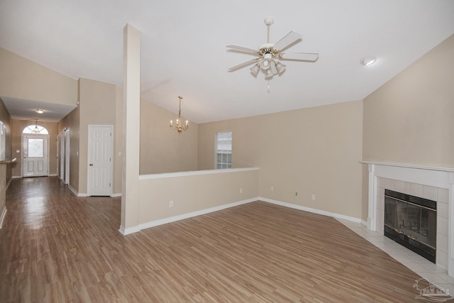 unfurnished living room featuring ceiling fan with notable chandelier, light hardwood / wood-style floors, vaulted ceiling, and a tiled fireplace