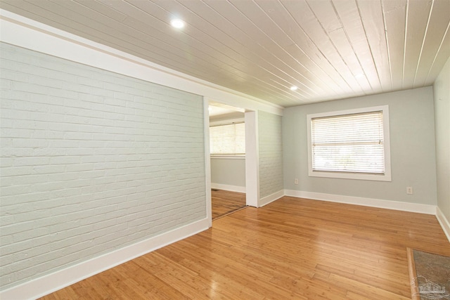 empty room with wood ceiling, brick wall, and light wood-type flooring