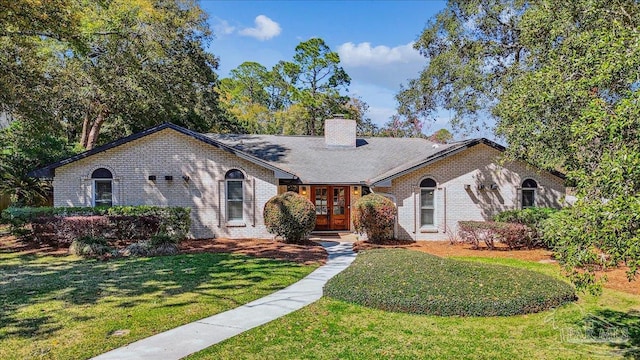 ranch-style house with french doors, brick siding, a front lawn, and a chimney