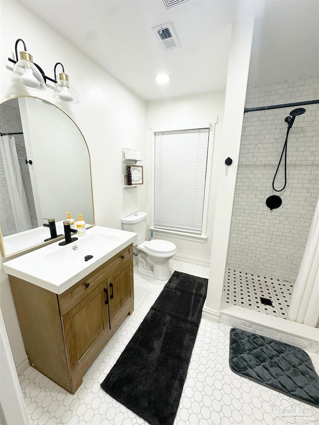 bathroom featuring vanity, toilet, baseboards, visible vents, and tiled shower