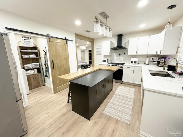 kitchen with a sink, a barn door, wall chimney exhaust hood, appliances with stainless steel finishes, and a center island
