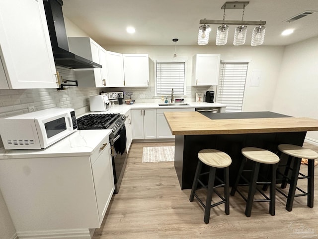 kitchen with butcher block countertops, stainless steel range with gas cooktop, a sink, wall chimney range hood, and white microwave