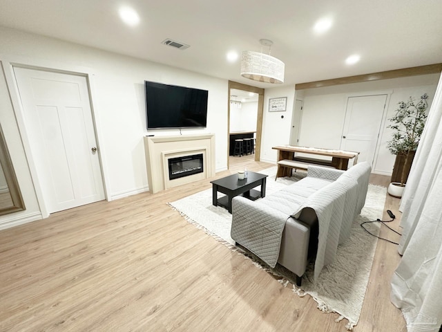 living area featuring recessed lighting, light wood-type flooring, baseboards, visible vents, and a glass covered fireplace