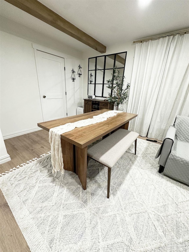 dining area with baseboards, beamed ceiling, and light wood-type flooring