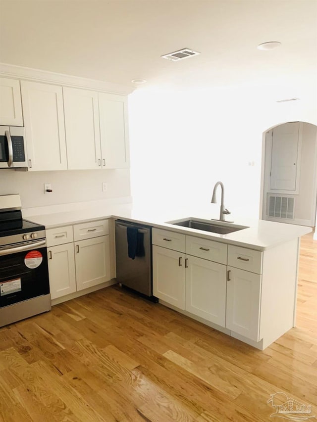 kitchen with white cabinets, appliances with stainless steel finishes, sink, kitchen peninsula, and light hardwood / wood-style flooring