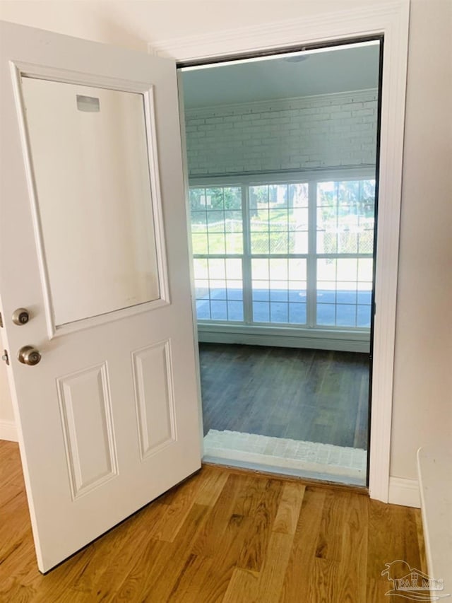 doorway with light wood-type flooring and brick wall