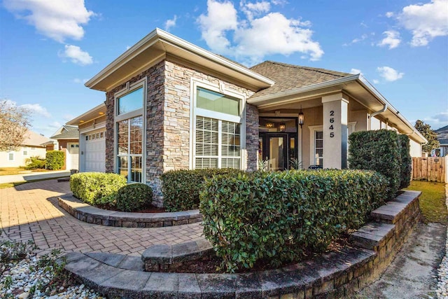 exterior space with an attached garage, fence, stone siding, decorative driveway, and stucco siding