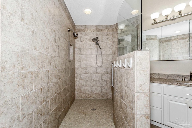 bathroom featuring a textured ceiling, tiled shower, and vanity