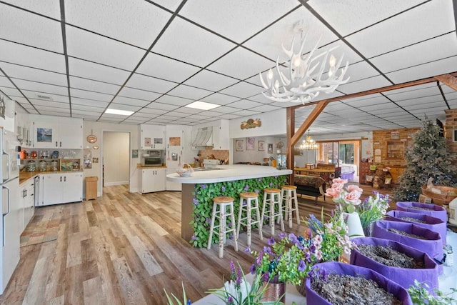 kitchen with light hardwood / wood-style floors, kitchen peninsula, white cabinetry, a chandelier, and a kitchen bar