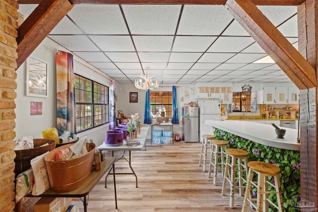 bar with a drop ceiling, stainless steel refrigerator, a chandelier, and light wood-type flooring