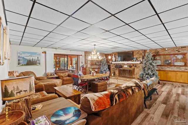 living room with a brick fireplace, a drop ceiling, an inviting chandelier, and light wood-type flooring