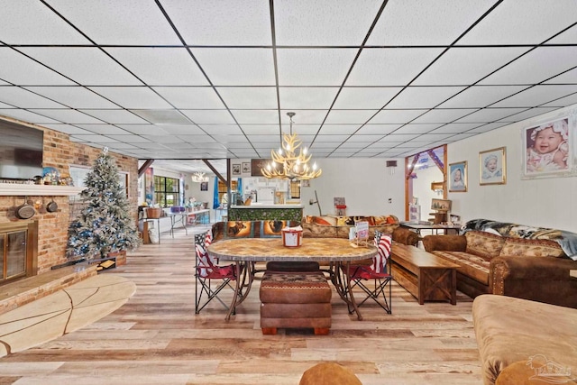 dining space featuring a drop ceiling, a brick fireplace, an inviting chandelier, and wood-type flooring