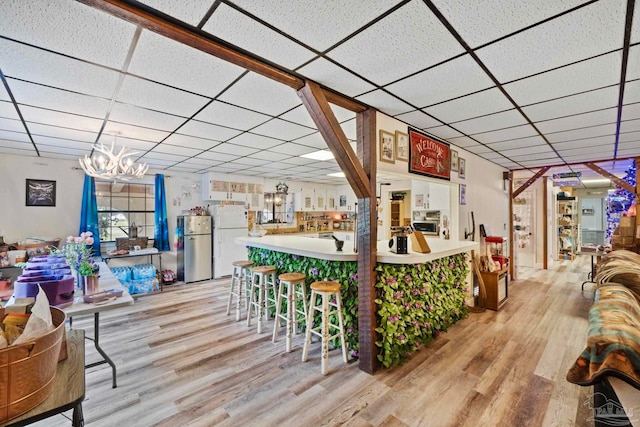 interior space featuring a paneled ceiling, a notable chandelier, and light wood-type flooring