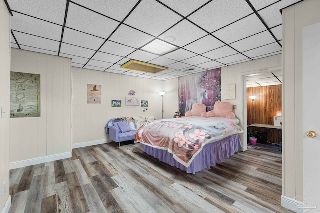 bedroom with hardwood / wood-style flooring, a paneled ceiling, and wood walls