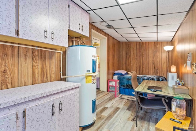 interior space featuring light wood-type flooring, a paneled ceiling, wood walls, and electric water heater