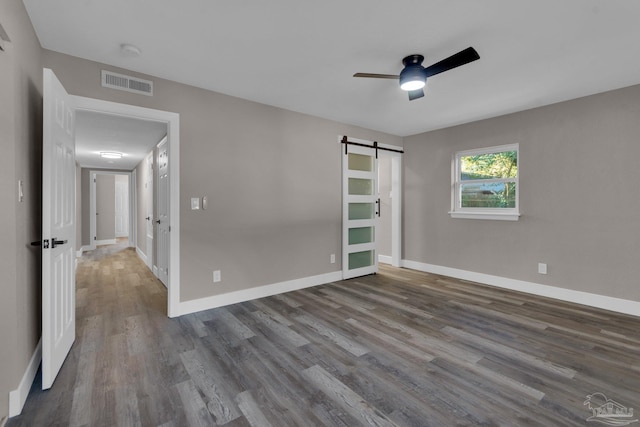 unfurnished bedroom featuring ceiling fan, dark hardwood / wood-style flooring, and a barn door