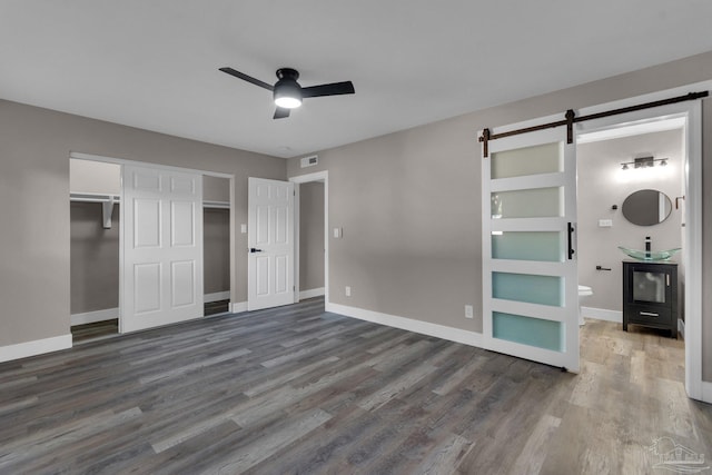 unfurnished bedroom with ceiling fan, a barn door, ensuite bath, hardwood / wood-style flooring, and a closet