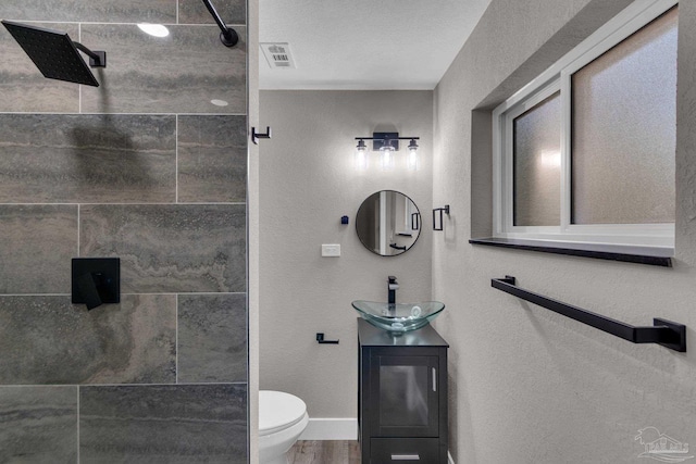 bathroom featuring toilet, a tile shower, wood-type flooring, and vanity