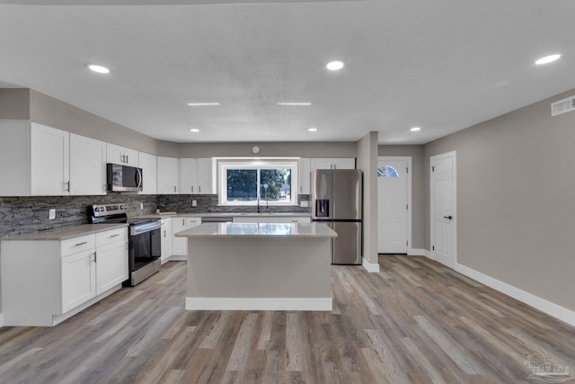 kitchen with stainless steel appliances, light hardwood / wood-style floors, white cabinetry, and light stone counters