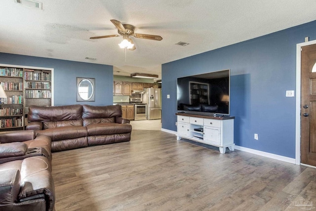 living room featuring light wood-style flooring, visible vents, ceiling fan, and a textured ceiling