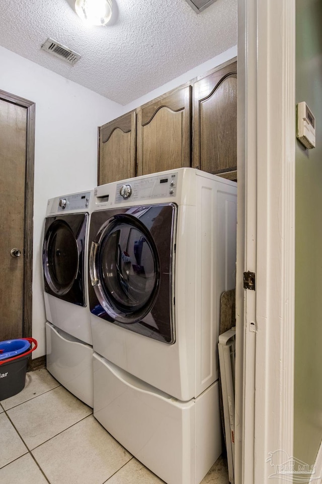 clothes washing area with light tile patterned floors, a textured ceiling, washing machine and dryer, visible vents, and cabinet space