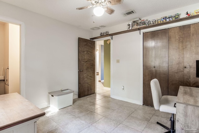 office with visible vents, ceiling fan, baseboards, and a barn door