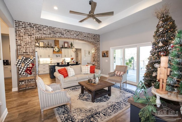 living room with dark hardwood / wood-style floors, ceiling fan, brick wall, and a tray ceiling